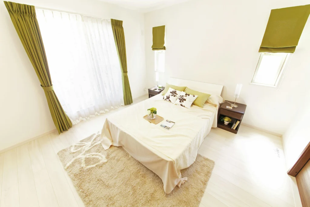 Image of bedroom with white walls, light wood floors, green accents, minimalist decor.