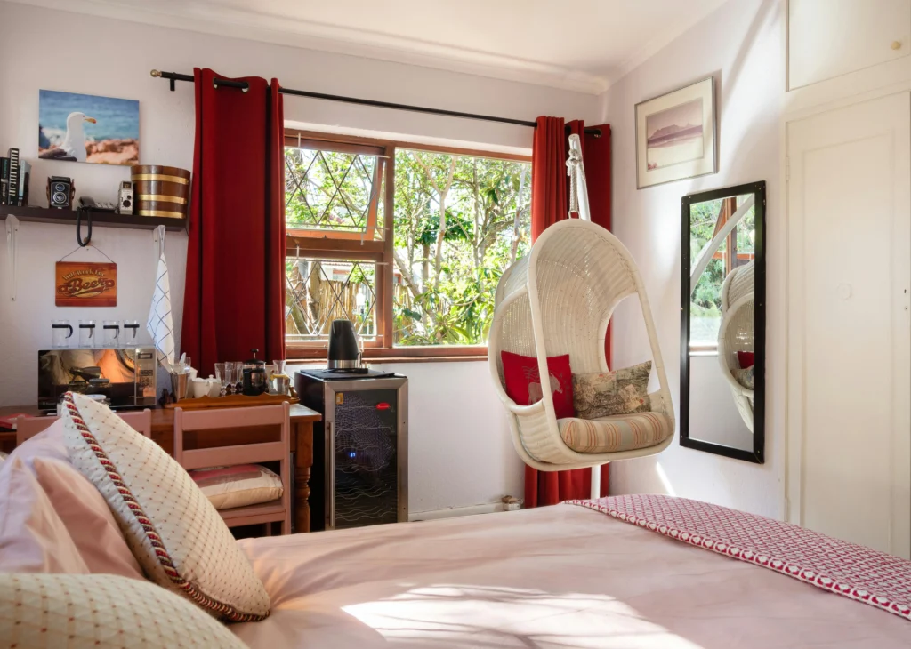Image of bedroom with quirky artwork, mini-fridge, hanging chair, pink bedding.