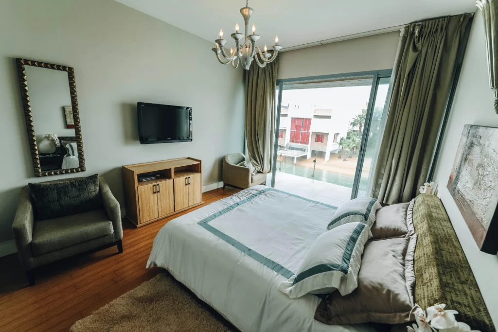 Image of bedroom with large sliding door, chandelier, armchair, neutral colors.